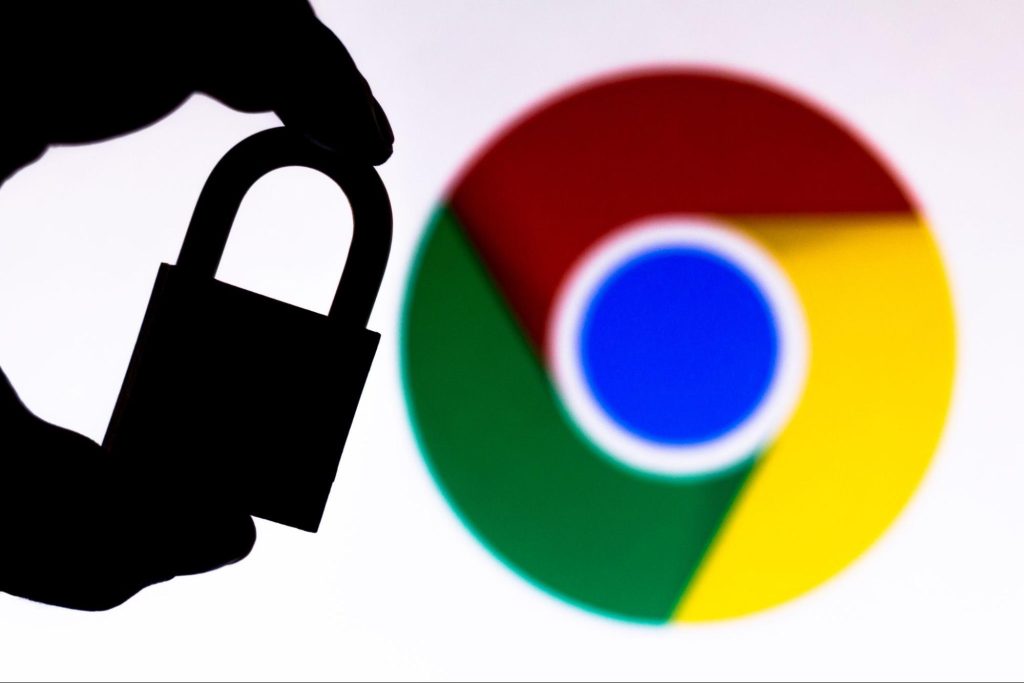 A silhouetted hand holding a padlock in front of the Google Chrome browser logo, representing cybersecurity or privacy concerns