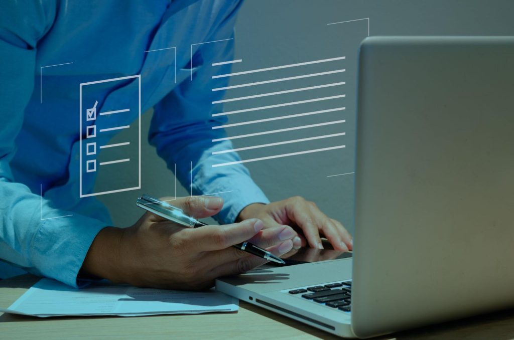 A man’s hand holding a pen and using the laptop, highlighting a checklist on the screen.
